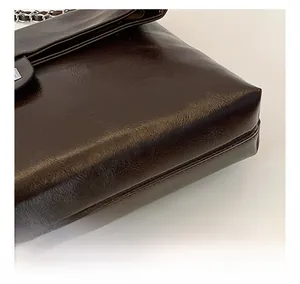 Detailed macro view of dark brown PU leather handbag with stitching and metal chain