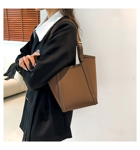 Brown leather tote bag featuring a structured trapezoid shape and adjustable shoulder strap