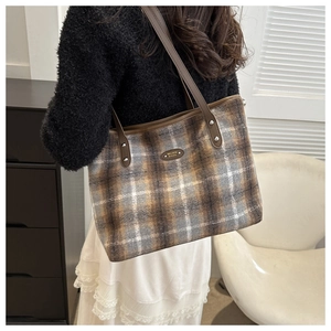 Detailed view of the plaid textured tote bag with leather strap and metal brand logo