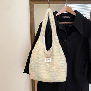 Detail of soft rainbow striped plush knit tote bag with brand label on dark coat background