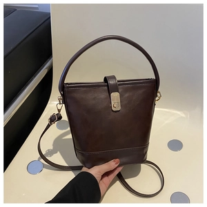 Detail einer dunkelbraunen Beuteltasche mit matter Textur und goldenem Drehverschluss