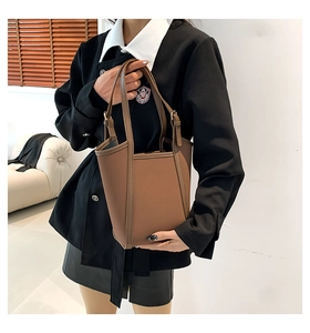 Detail view of the brown PU leather bucket bag with minimalist dual handles on a white sofa