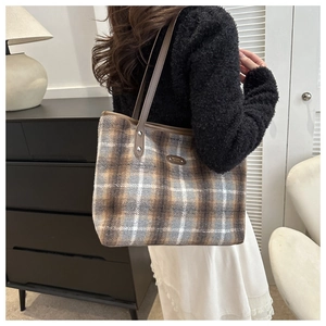 Detail of a large wool-textured checkered tote bag worn over the shoulder by a model