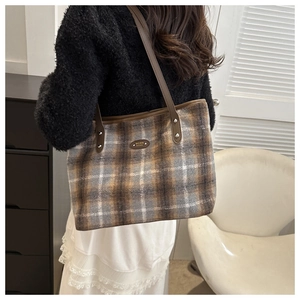 Detail of checkered tote bag with brown leather strap and metallic brand logo plate