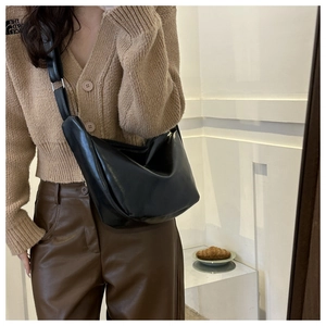 Model wearing a black glossy patent leather hobo crossbody bag with adjustable strap