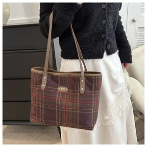 Detail of red and green plaid wool tote bag featuring brown leather straps and metal logo