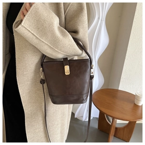 Detail der dunkelbraunen Eimertasche aus PU-Leder mit verstellbarem Gurt am beigen Mantel