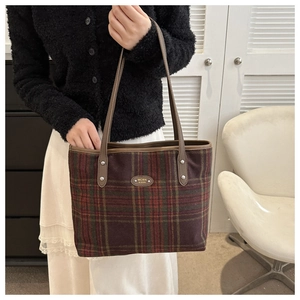 Detail of checkered tote bag with metal nameplate and leather handles in a home setting