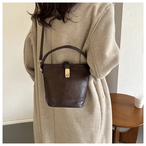 Detail einer dunkelbraunen Vintage-Beuteltasche mit Goldschnalle zu einem beigen Wollmantel