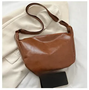 Detailed view of brown PU leather crossbody bag with silver buckle and phone for scale