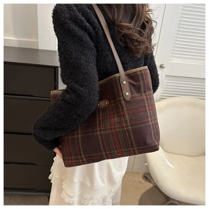 Close-up of vintage plaid tote bag with brown leather straps and metal logo detail