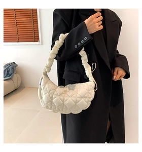 Close-up of a white quilted cloud bag with ruched strap worn over a black winter coat