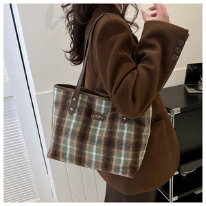 Detail of checkered wool tote bag with leather trim and metal logo on a wool coat