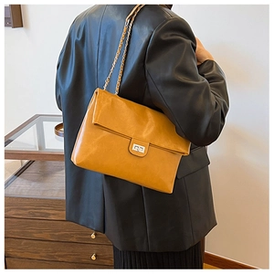 Detail of mustard yellow leather shoulder bag with silver turn-lock and woven chain strap