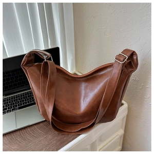Detail of a brown crescent-shaped faux leather bag with glossy oil finish and silver buckle