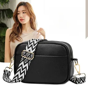 Detail of black lychee leather crossbody bag with geometric woven strap and gold zipper