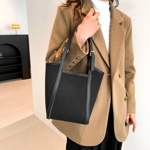 Minimalist black tote bag with leather trim and gold buckles held by a model