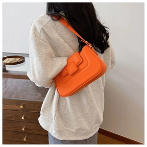Fashionable bright orange PU leather underarm bag worn by a model in a cozy indoor setting