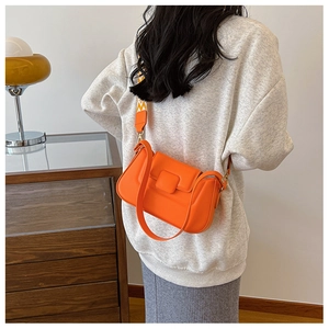 Detail of orange square crossbody bag with textured geometric strap and golden hardware