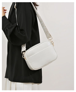 Detail view of white pebbled leather camera bag with golden hardware and woven strap