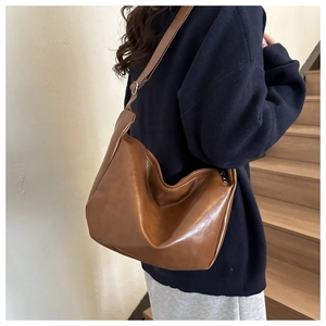 Brown PU leather hobo bag with adjustable strap worn by model on a white staircase