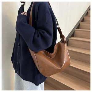 Detail of minimalist brown PU leather dumpling bag with adjustable strap and sleek zipper
