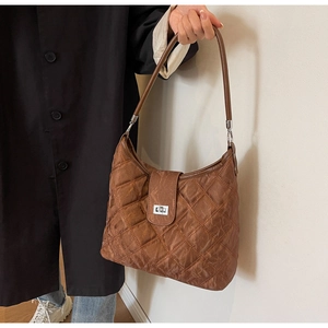Detail of a brown quilted hobo bag with silver twist lock held by a model in a black coat