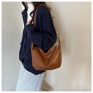 Detail of a dark brown PU leather hobo bag worn with a navy cardigan and grey skirt
