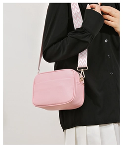 Pink pebbled leather crossbody bag with colorful woven strap shown on a model