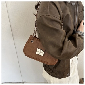 Detail of brown crocodile pattern shoulder bag with silver chain strap and metal buckle