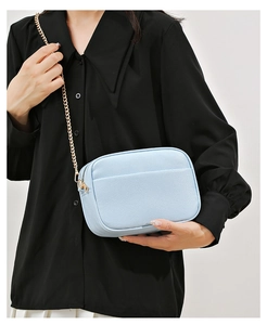 Detail of light blue pebble grain leather camera bag with gold chain strap on model