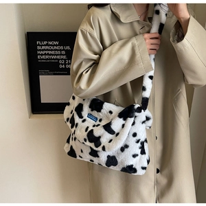 Detail of plush crossbody bag featuring black and white cow print and blue designer label