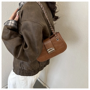 Detail of a brown crocodile pattern shoulder bag with a silver chain and metal buckle