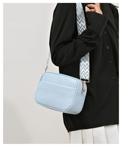 Close-up of sky blue lychee leather camera bag with colorful geometric woven strap