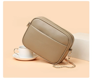 Macro detail of taupe camera bag showing lychee grain leather texture and gold hardware