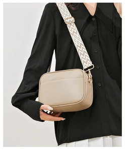 Detail of beige pebble leather camera bag with stylish geometric wide strap on a model