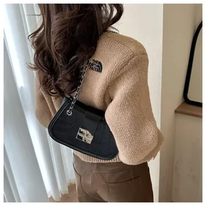 Detail of black crocodile texture shoulder bag with silver metal chain on female model