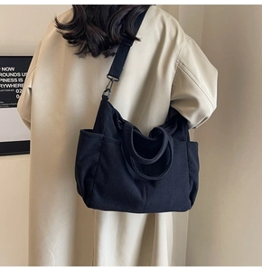 Detail view of black corduroy crossbody bag showing side pocket and woven shoulder strap