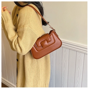 Close-up of a brown leather shoulder bag with a square buckle detail on a model