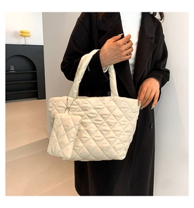 Close-up of quilted cream tote bag featuring a handheld strap and handmade logo tag