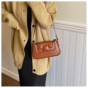 Caramel brown leather baguette bag styled with beige knit cardigan and black skirt
