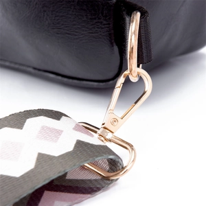 Detail of black crossbody bag with golden lobster clasp and colorful woven shoulder strap