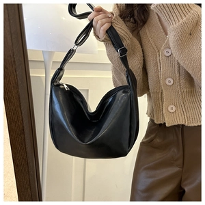 Detail shot of a black PU leather half-moon bag held by a model in autumn outfit