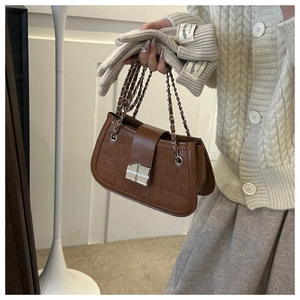Detail of brown crocodile pattern PU leather handbag with silver metal lock and chain strap