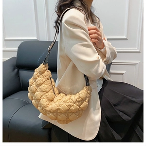 Borsa a luna trapuntata beige con tracolla in pelle nera indossata da una modella in studio