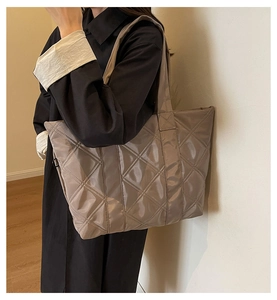 Detail of glossy quilted tote bag with wide shoulder strap in dark taupe finish