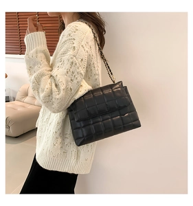 Détail du sac bandoulière matelassé noir avec chaîne dorée sur un mannequin en pull blanc