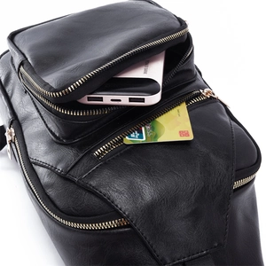 Detail view of black textured leather bag with multi-zipper layers holding power bank and cards