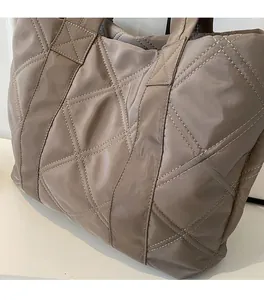 Close-up detail of the quilted diamond pattern and glossy nylon fabric on the taupe tote bag