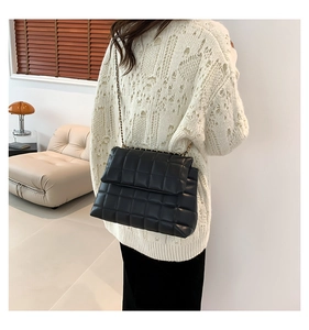 Détail d'un sac bandoulière noir matelassé avec chaîne dorée élégante porté par un mannequin